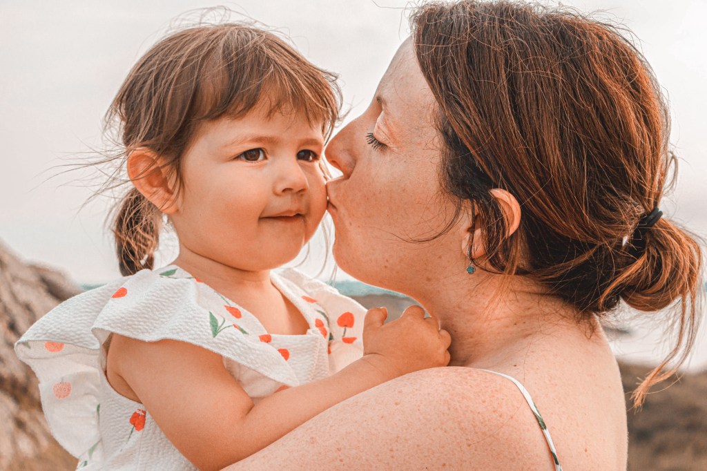 Portrait de jeune maman embrassant sa fille, bord de mer
